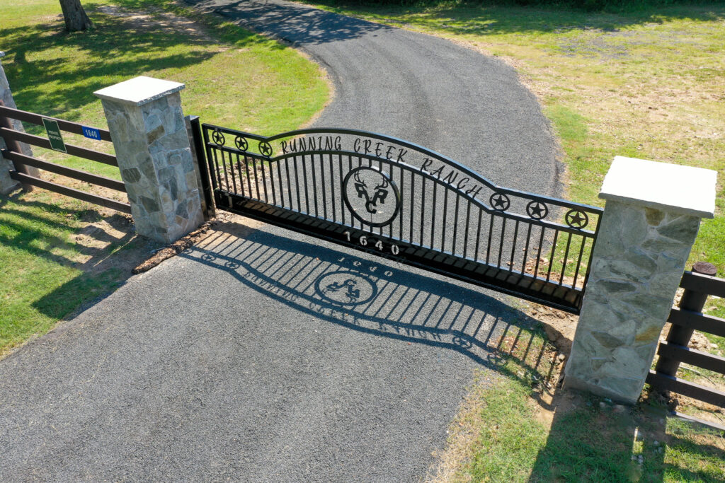 Custom black gate with a deer in center and with stone columns on each side of the gate.