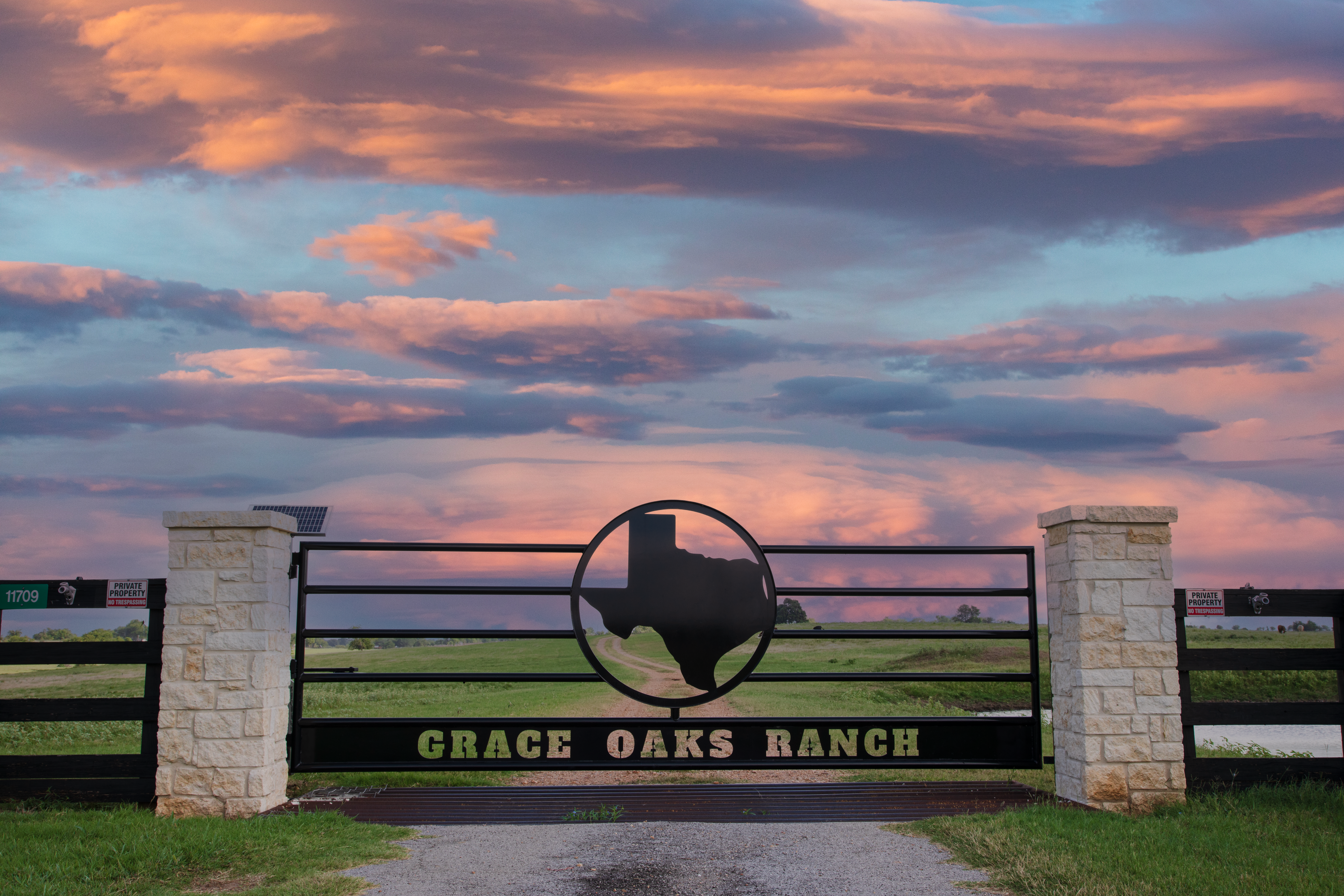 Texas themed metal gate with oversized Texas shape in the center pairs with two stone columns and solar powered operator