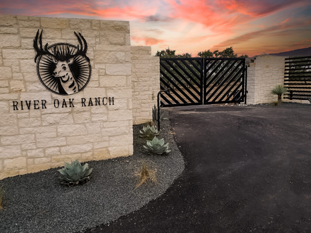 White stone columns with decorative metal deer to accent the black custom double swing gate