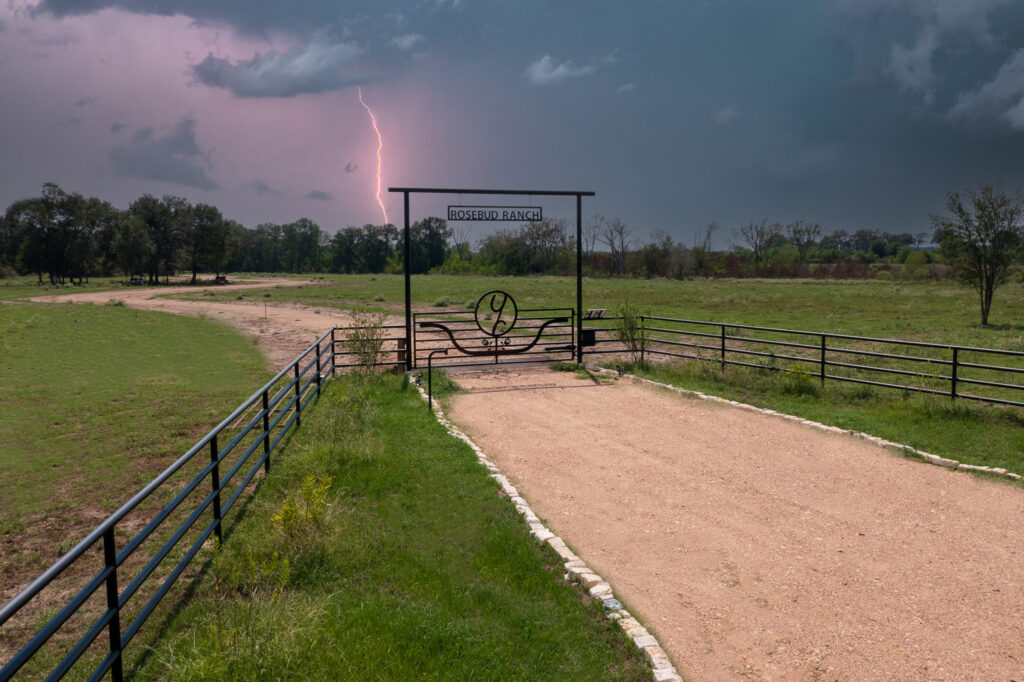Storm rolling through area and lighting striking in the background of a custom ranch entrance with metal roses in the center.