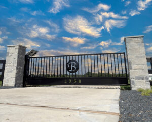 Stone columns with a swing gate between them with a circle and a letter B in the middle of gate.