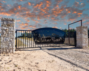Custom swing gate with deer scene in the center of the gate with two stone columns on the side of the gate.